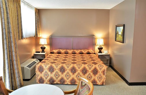 Interior of a hotel room at Hotel PG, showcasing a bed, chair, and table for a pleasant stay.