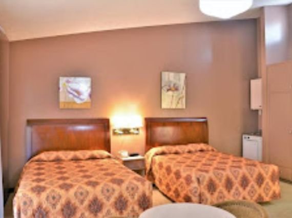 A motel room at Hotel PG featuring two beds and a lamp on one side, creating a cozy and inviting atmosphere.
